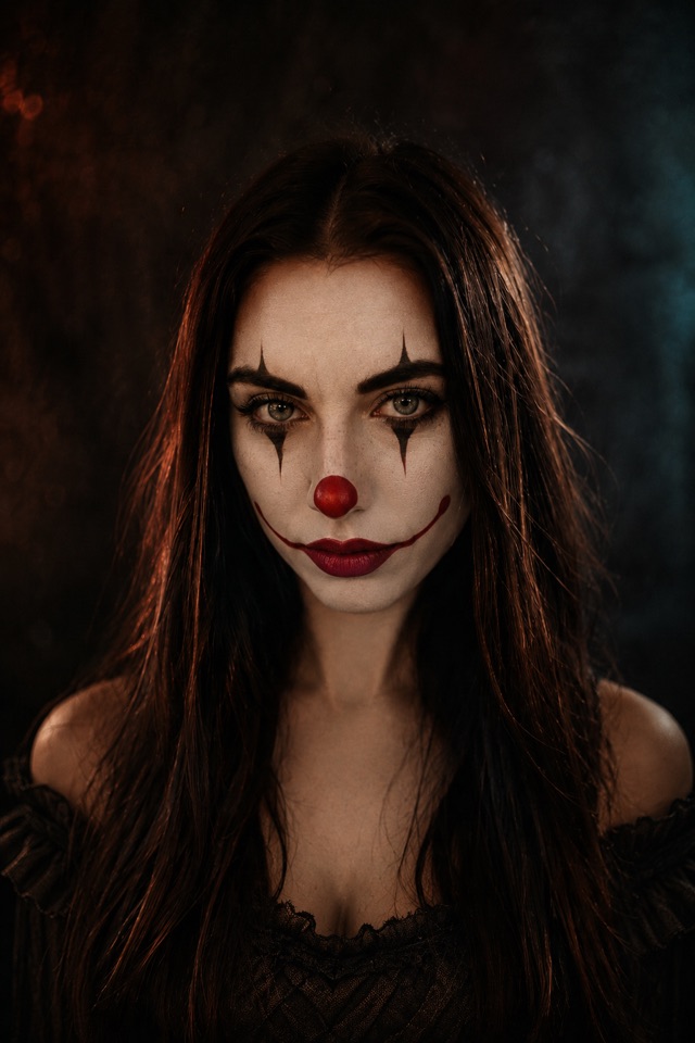 A dancer in freak show face paint under the bulbs