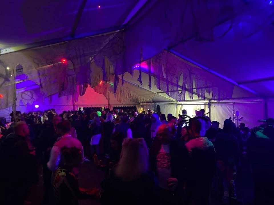 A packed marquee bar hung with cobwebs under pink and purple light